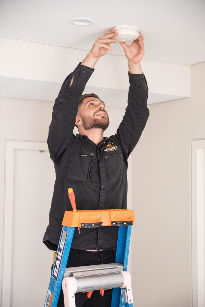 A man standing on a ladder, fixing a ceiling fan in a home.