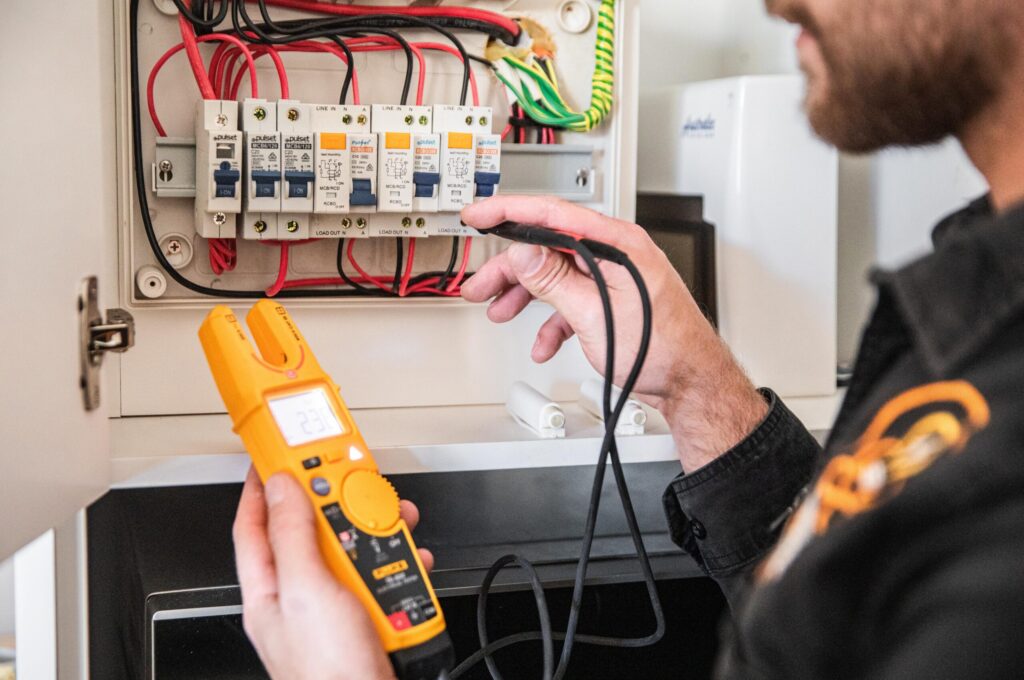 A man using a multimeter to check an electrical panel for any electrical issues or abnormalities.